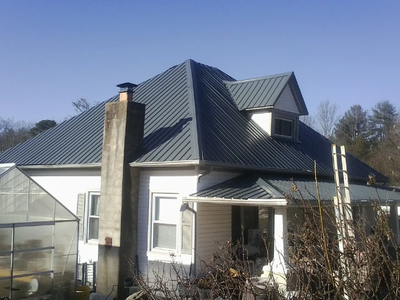 Dark blue standing seam metal roof on a white farmhouse with dormer — Slate & Tile Roof Repair by Roofing Brothers in Horton