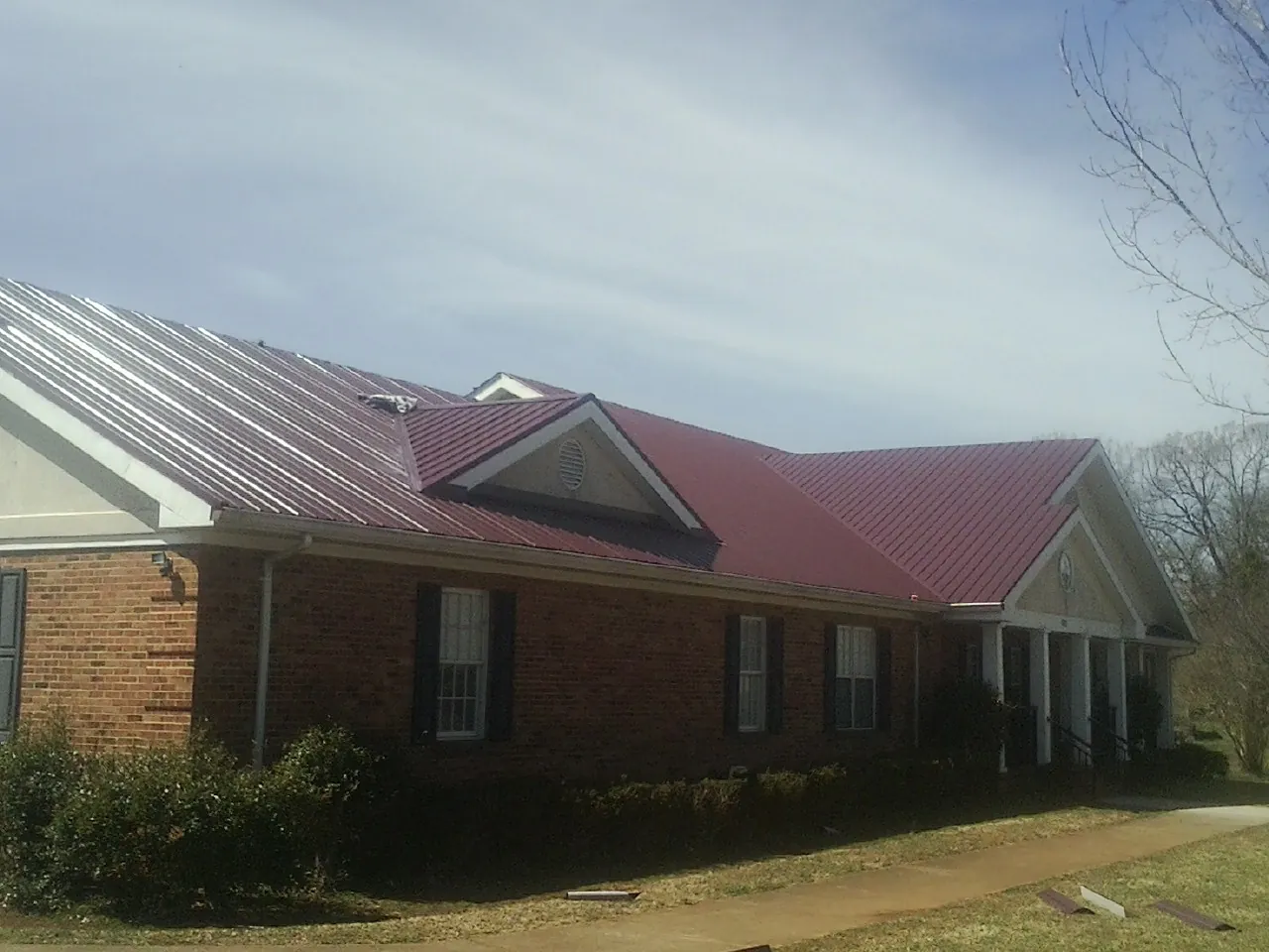 Red metal roof with gabled entries on a long brick building, from a Hail Damage Roof Repair job in Horton