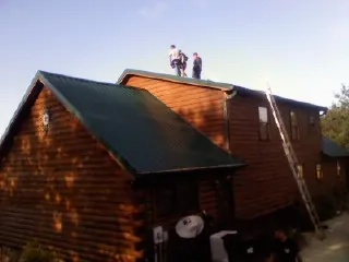 Crew on the ridge of a green metal roof on a two story log home in Horton
