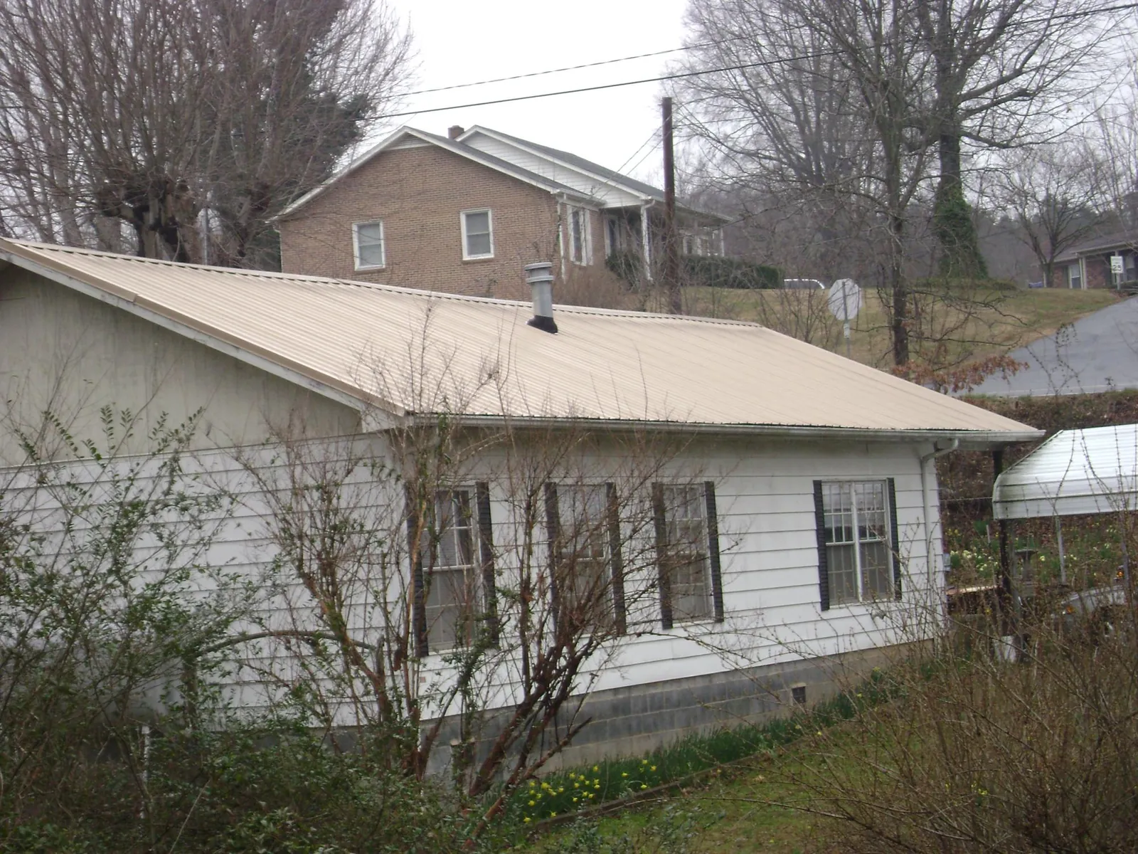 Tan metal roof on a white sided house set into a hillside — Commercial Roofing by Roofing Brothers in Horton