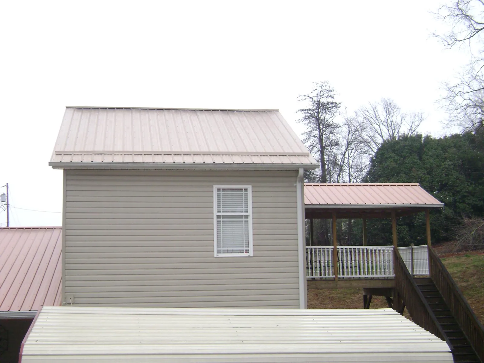 Tan metal roofs on a two story addition and attached porch, from a Roof Replacement job in Horton